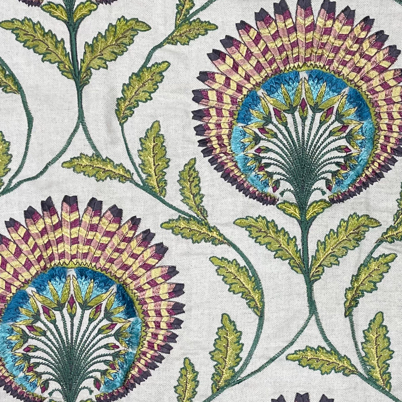 Close-up of Ann Gish Tavus pillow fabric with embroidered botanical medallions in plum, teal, and olive.
