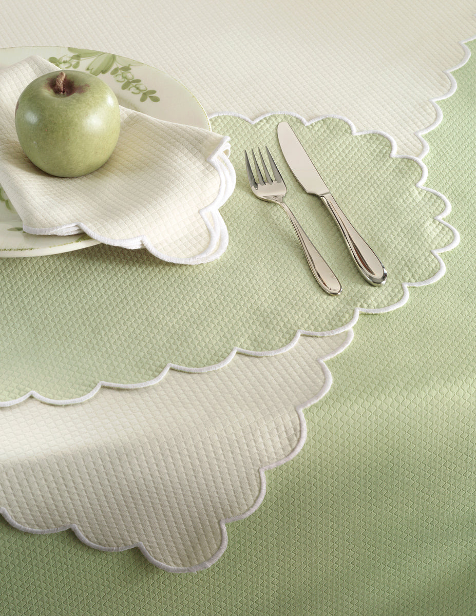 A green apple on a plate with a matching napkin, alongside a fork and knife, rests on Matouk’s Savannah Gardens Placemat Set in pale green and cream diamond pique.