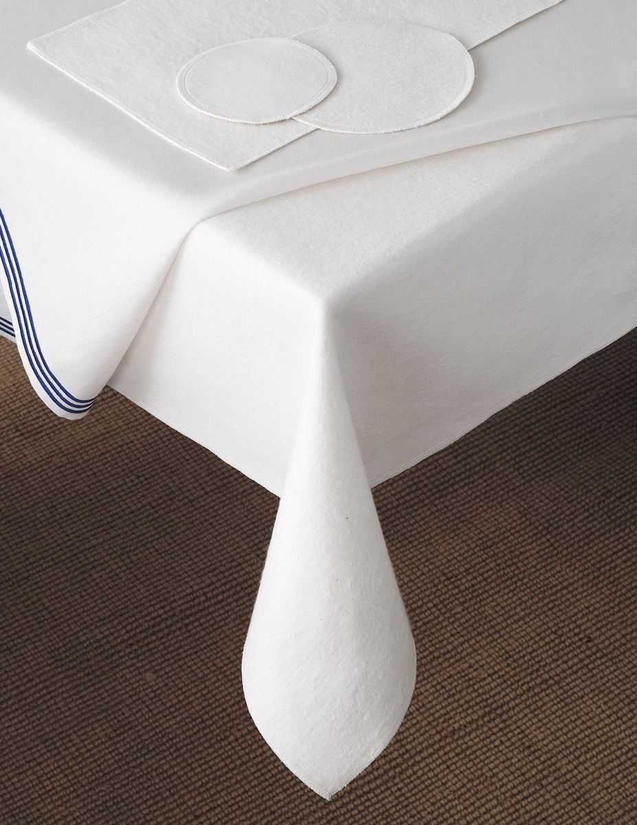 A white table with Matouk Silencer Padding—felt-like, heat-resistant tablecloth—plus matching round placemats and coasters, all edged with stripes.