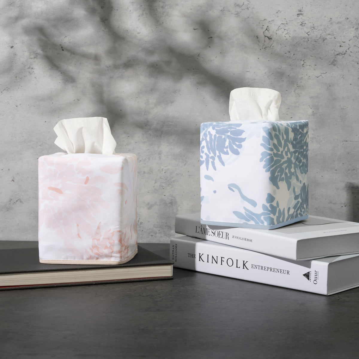 Two Matouk Chrysanthemum tissue box covers in blush and slate blue floral, styled on books.