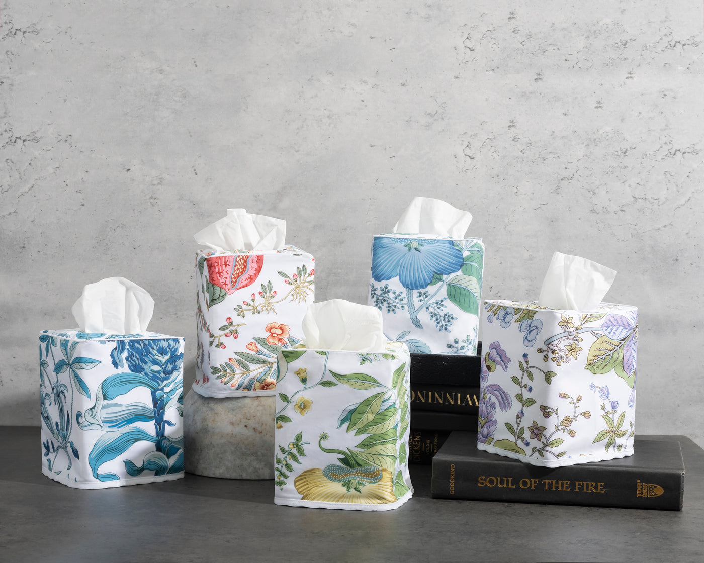 Close-up of six Matouk floral linen tissue box covers in varied botanical prints, styled with books.
