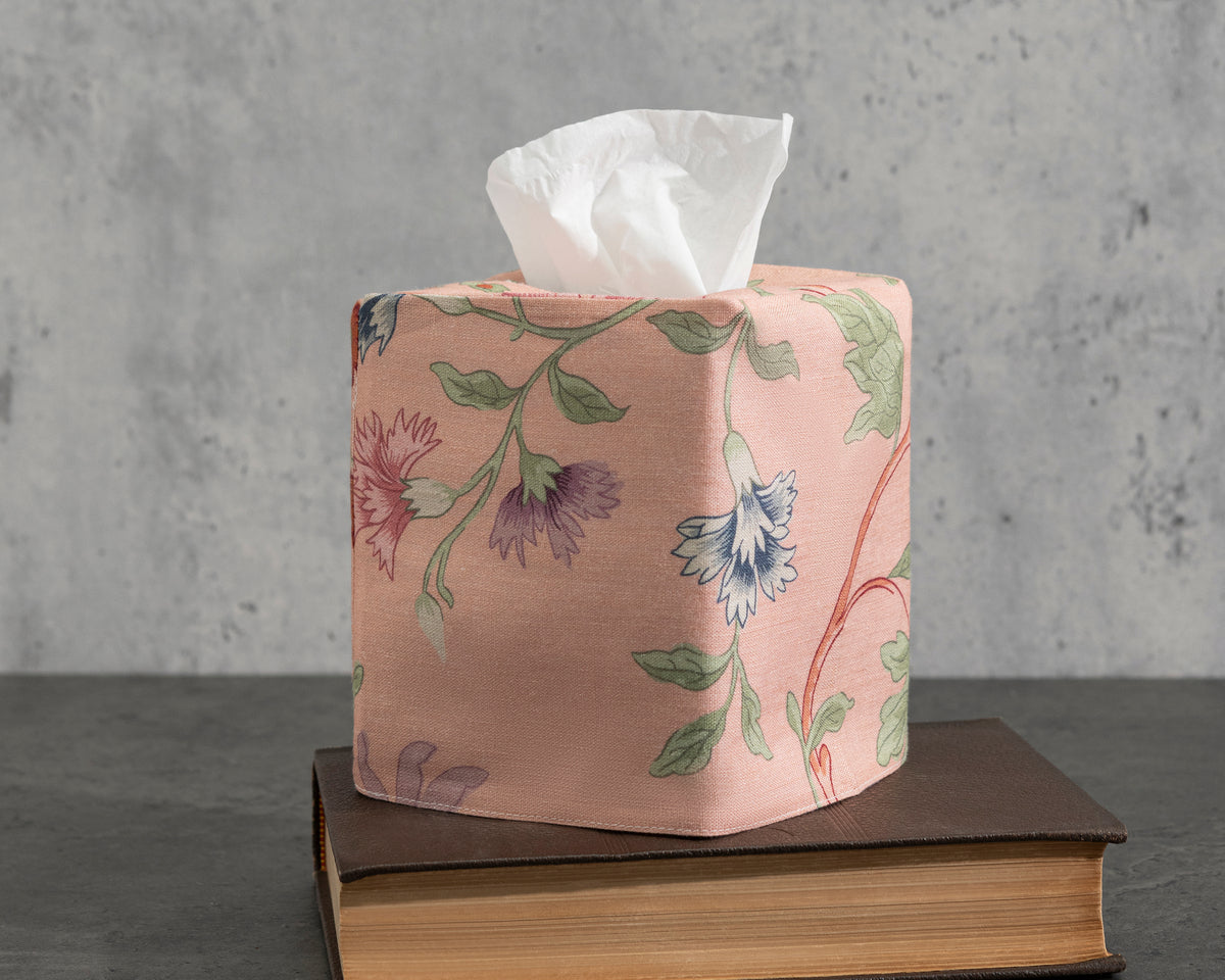 The Simone Tissue Box Cover by Matouk sits atop two stacked books, displayed against a gray textured background.