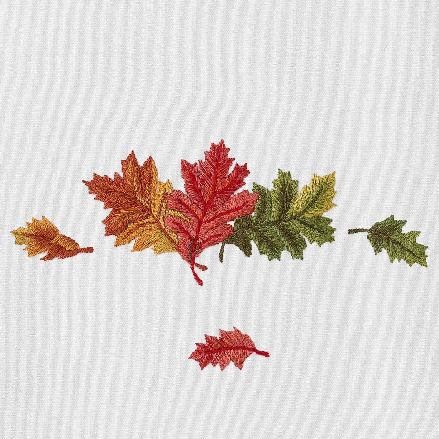 Close-up of embroidered autumn leaves in red, orange, and green on white linen.