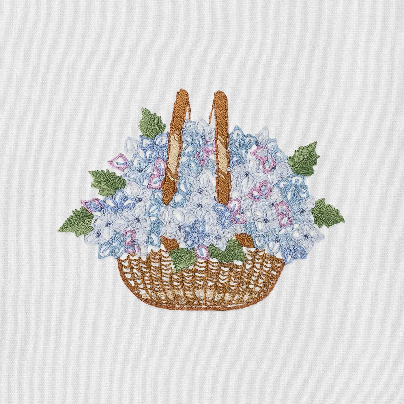 Close-up of embroidered wicker basket with blue hydrangeas and green leaves on white linen.