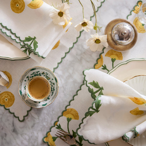 Matouk Gisele ivory linen placemats with yellow floral embroidery, styled with teacup and white cosmos.