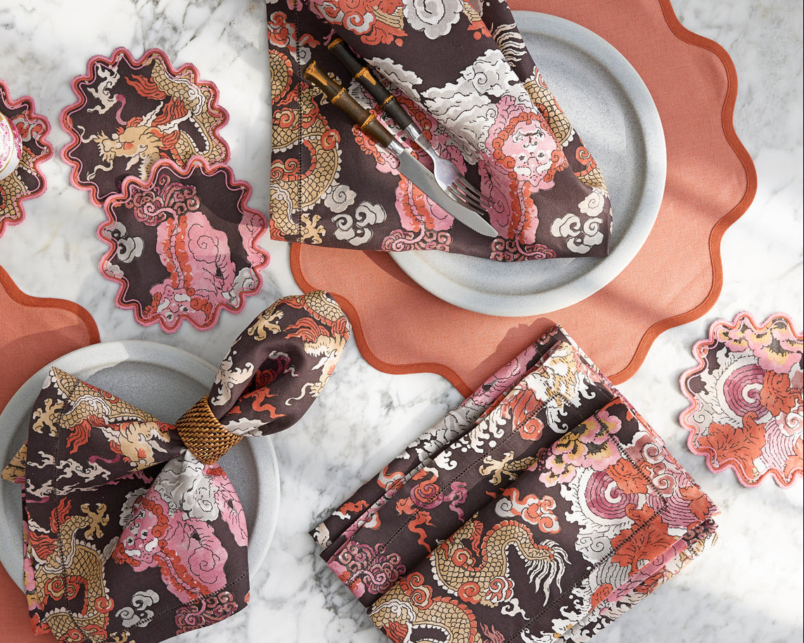 Set a unique tablescape with Matouk's Scallop Edge Placemat Set, styled with matching coasters, cutlery, bow-tied napkins on white plates, all atop a marble surface for a sophisticated look.