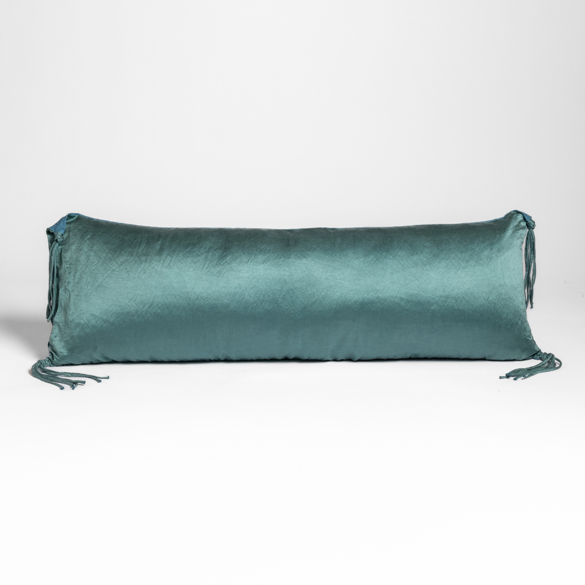 Long Cenote velvet bolster pillow with tassel ties at each end, on neutral background.