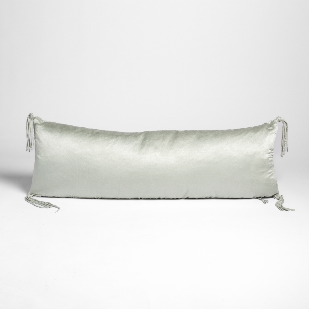 Elongated Cloud silk throw pillow with tassel ties at each end, on neutral background.