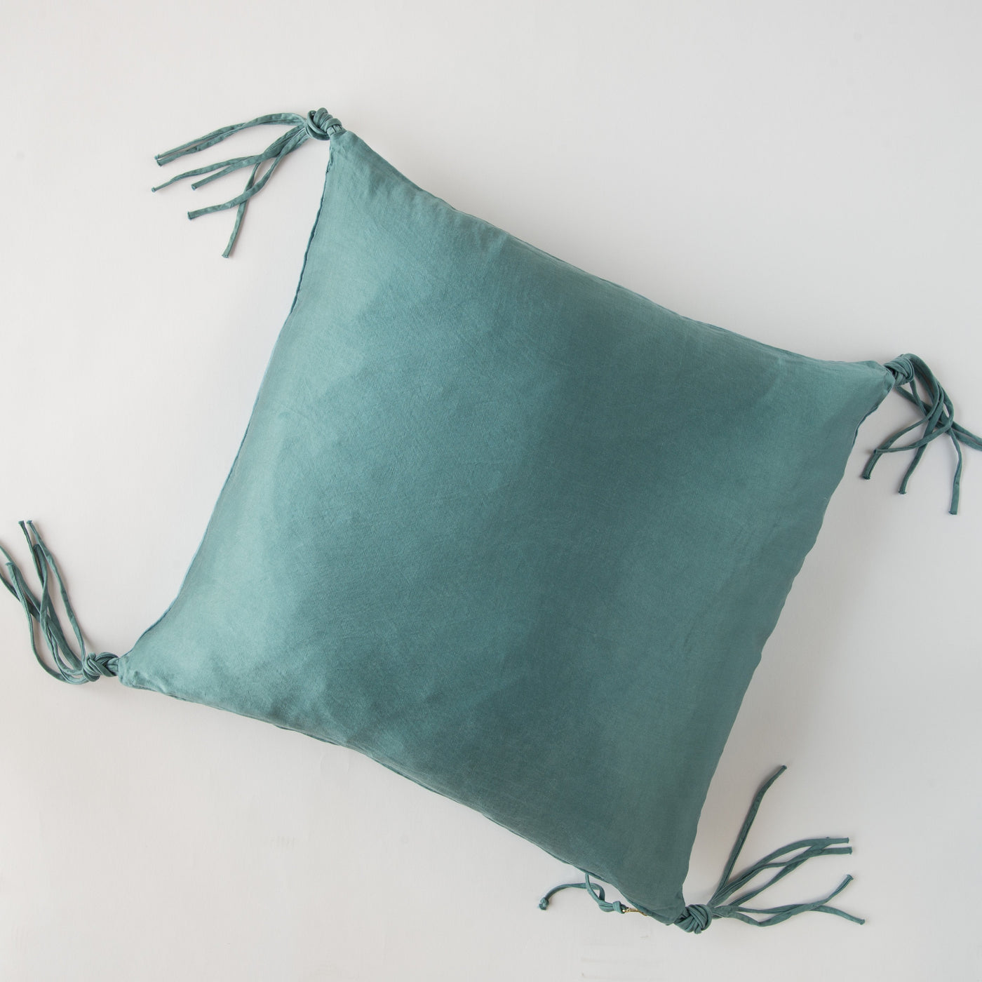 Cenote silk-look throw pillow with knotted tassel ties at all four corners, flat lay view.