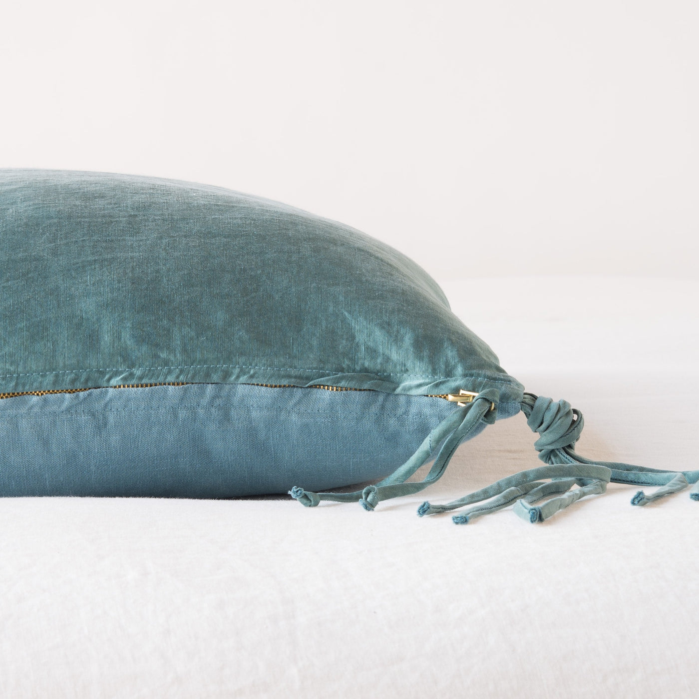 Side view of Cenote Bella Notte Taline throw pillow showing gold zipper and knotted tassel ties.