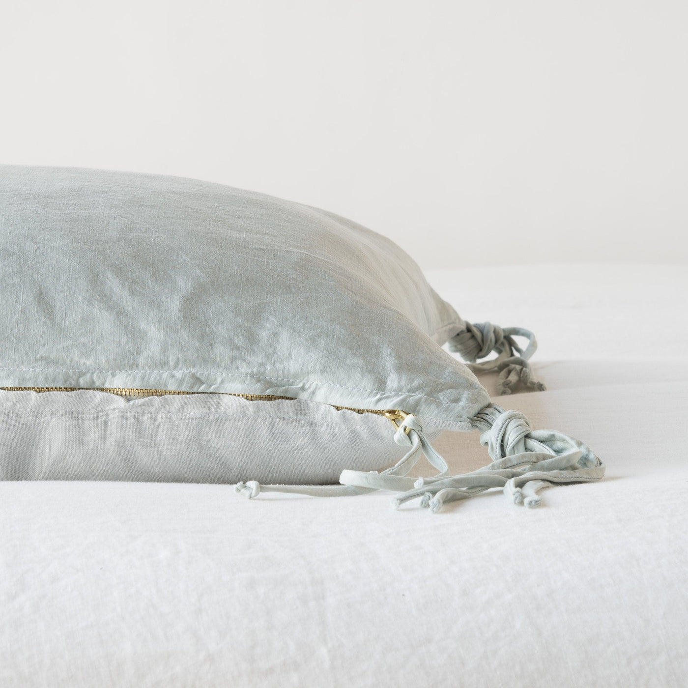 Side view of Cloud Taline pillow showing gold zip detail and knotted tassel trim against white bedding.