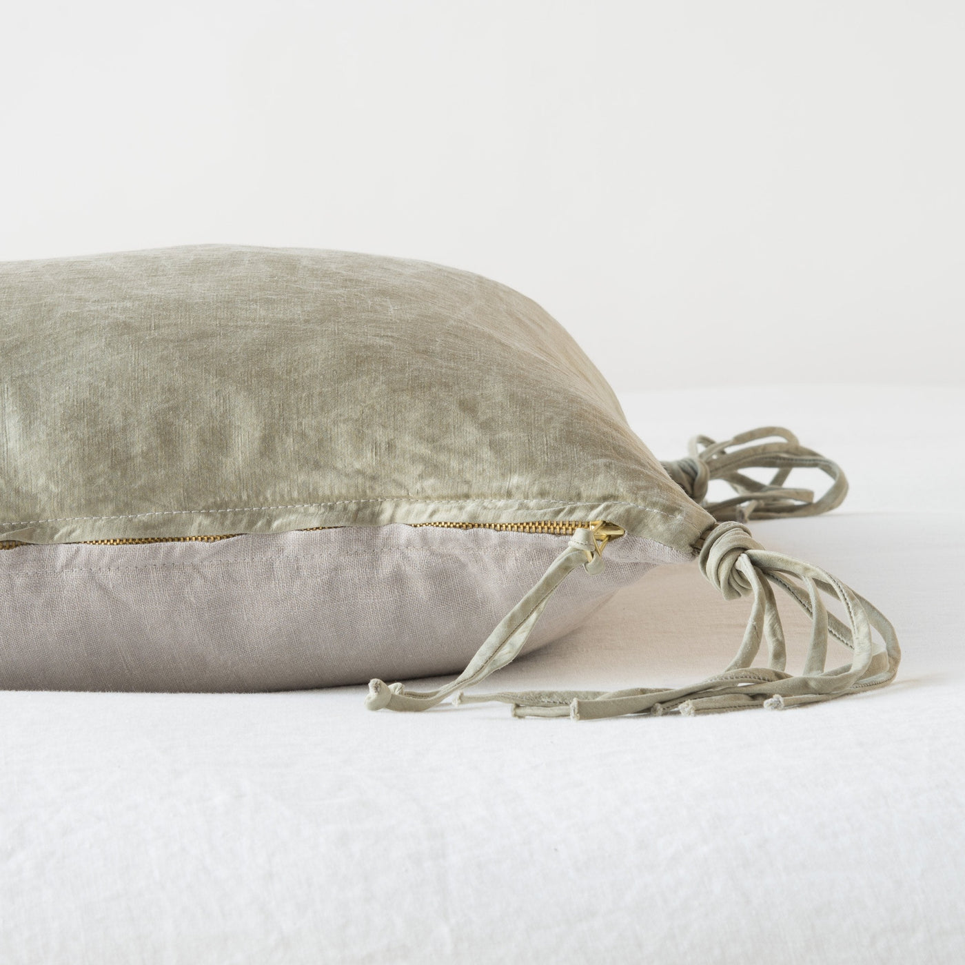 Side profile of Fog velvet throw pillow showing gold zipper closure and knotted tassel tie detail.