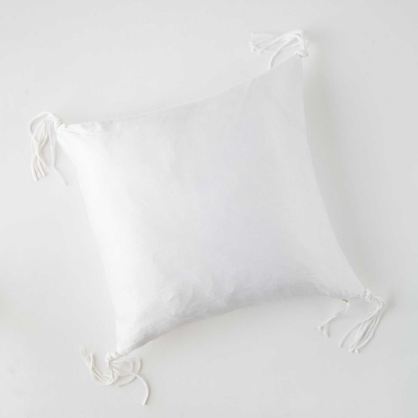White linen throw pillow with knotted tassel ties at all four corners.