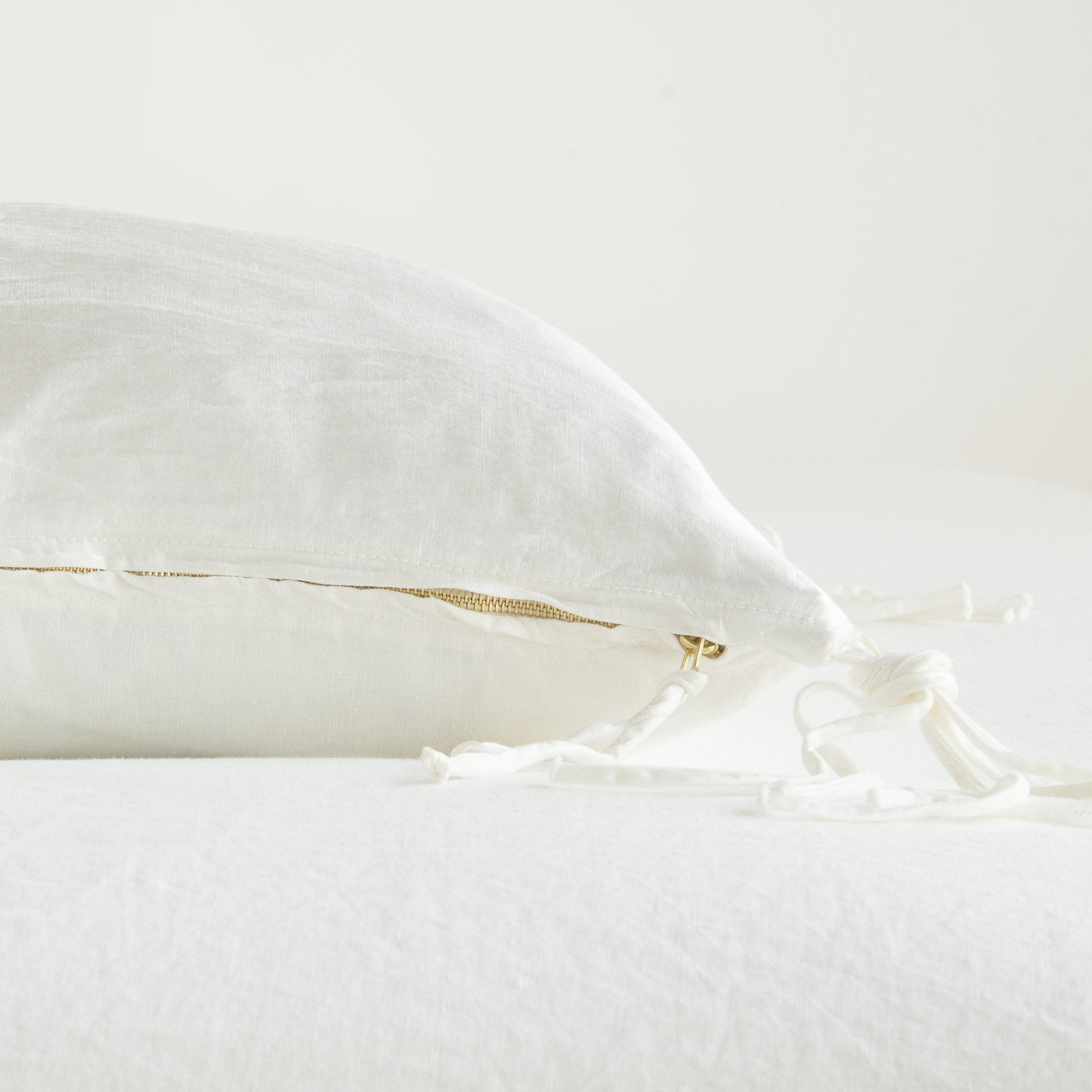 Side profile showing gold zipper closure and fringe tassel trim detail in Winter White linen.
