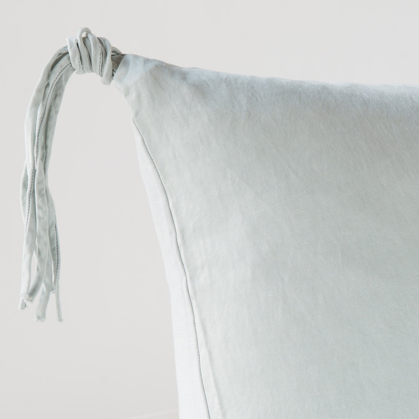 Close-up of Bella Notte Taline sham corner in Cloud, showing knotted tassel tie detail on soft linen.
