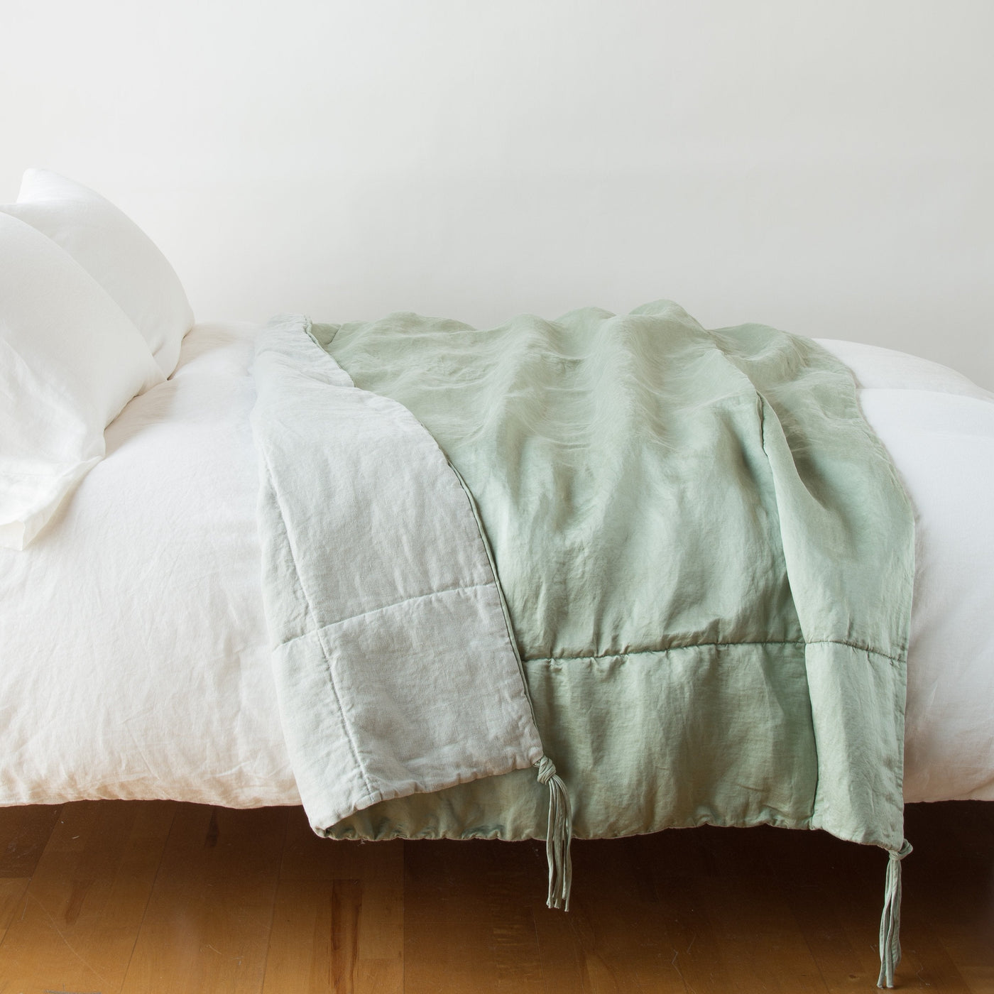 Eucalyptus linen blanket with tassel ties draped across a white bed, reverse in natural.