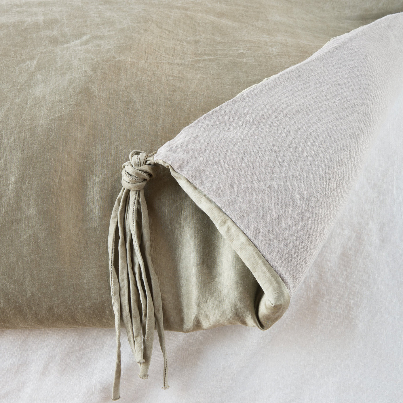 Close-up of Fog Bella Notte Taline blanket corner with knotted tassel fringe detail on linen fabric.