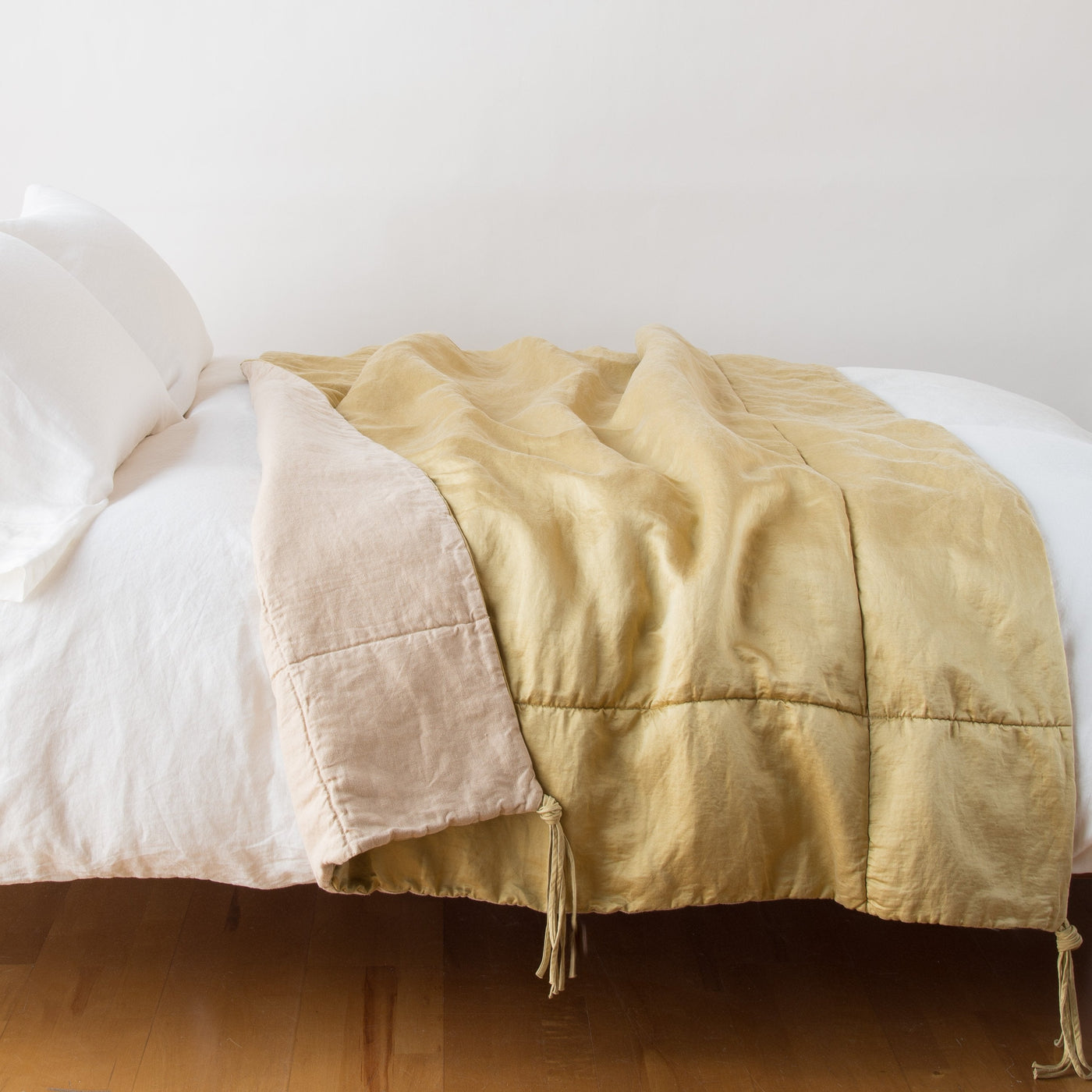 Honeycomb linen blanket draped over bed, showing reverse blush side with corner tassel detail.