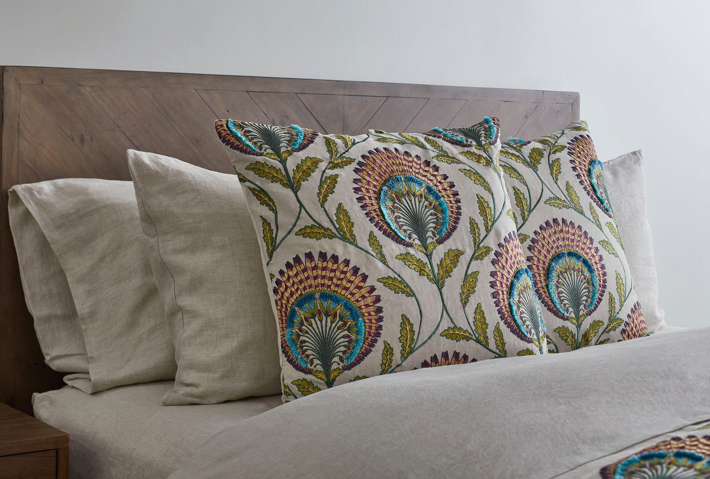 Ann Gish Tavus pillow with multicolor floral embroidery styled on a neutral linen bed.