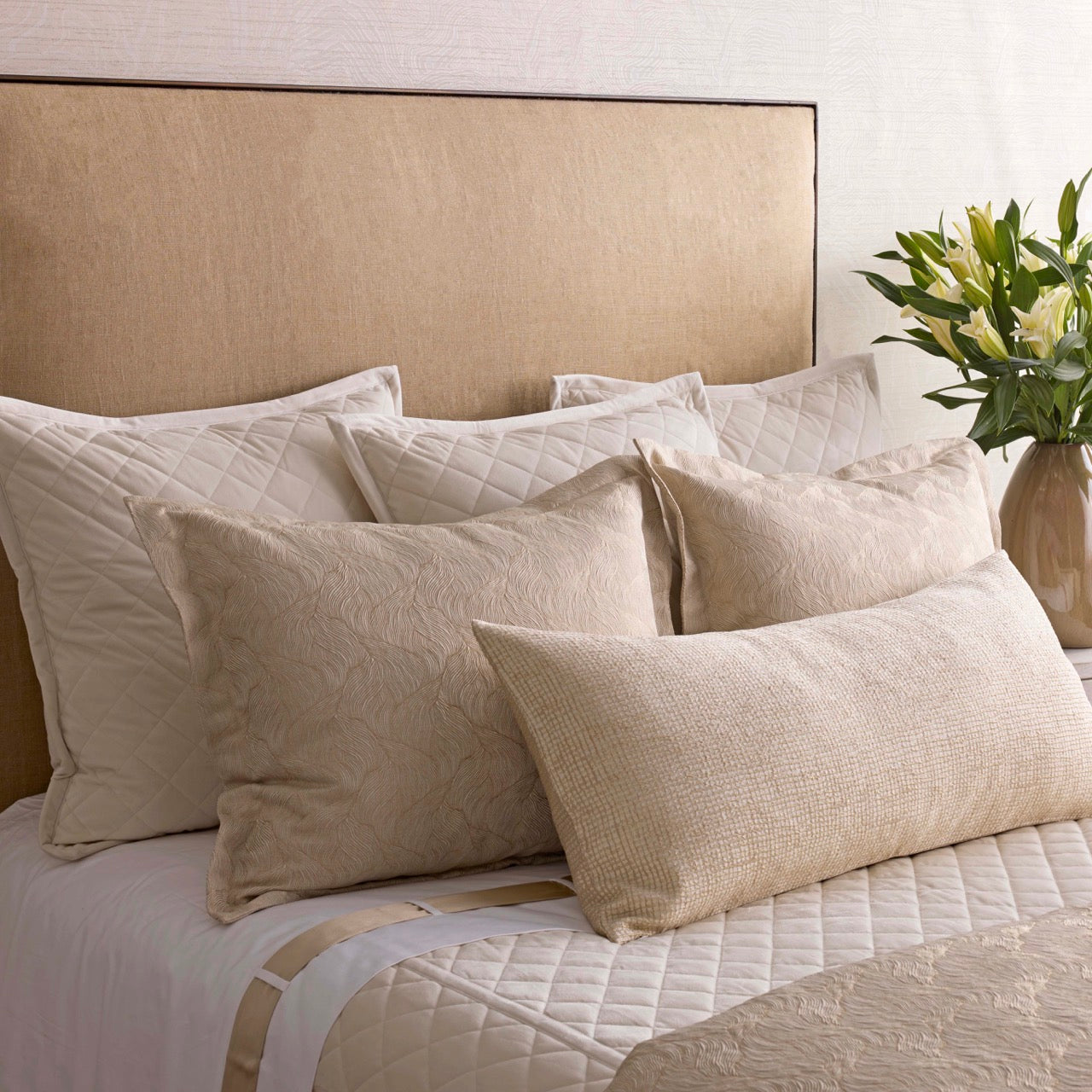 Layered champagne quilted and textured pillow arrangement on a styled bed.