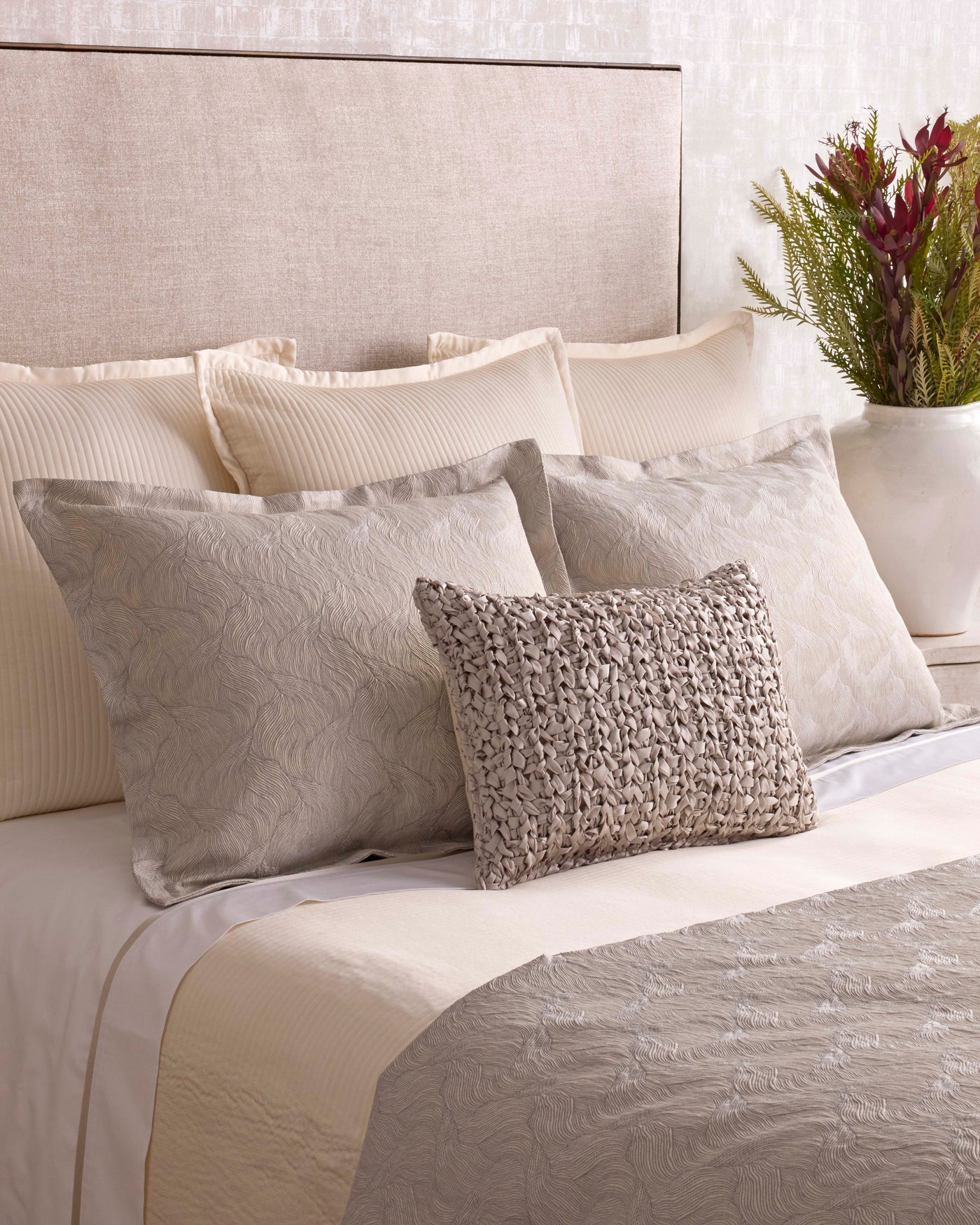 Taupe textured accent pillow styled on a bed with matelassé shams and layered neutral bedding.