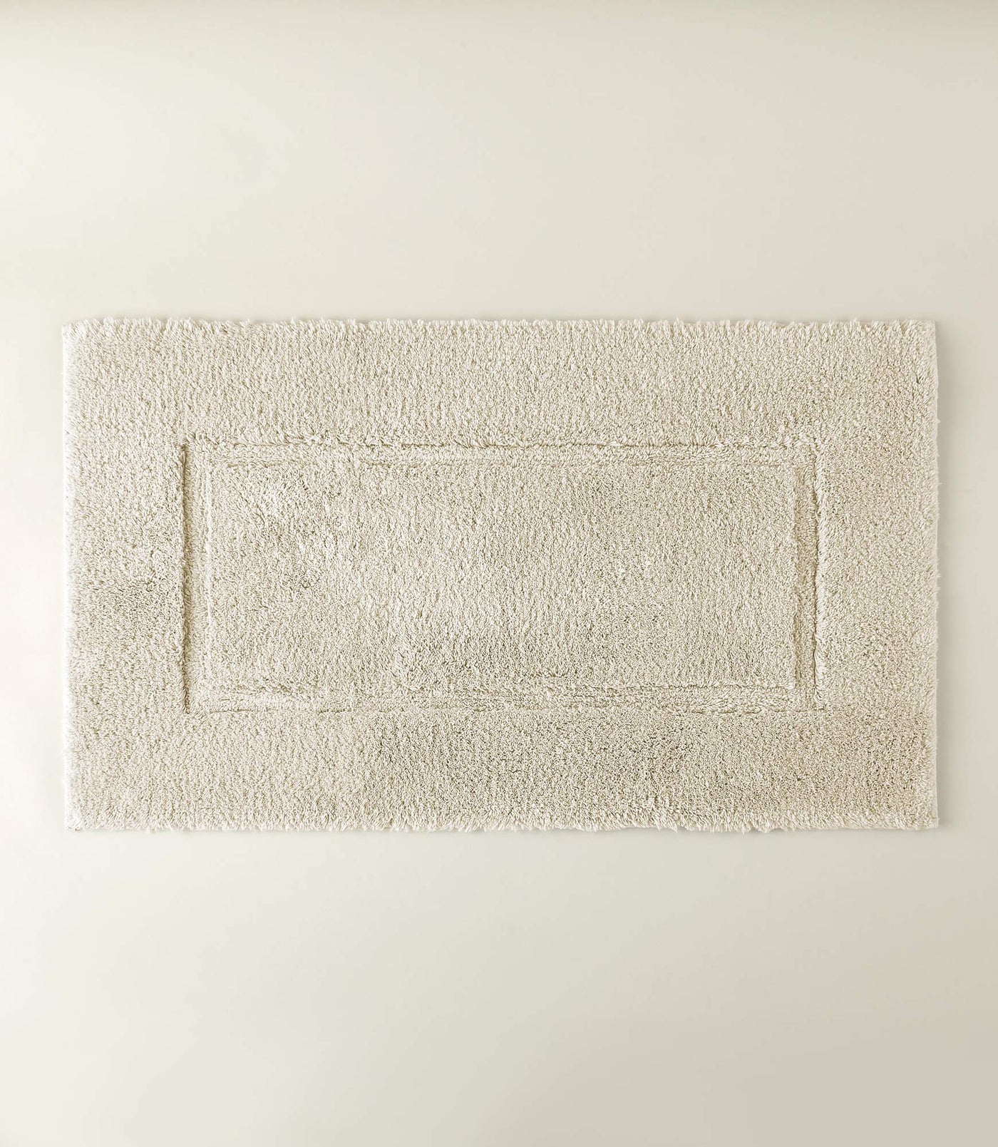 Ivory tufted bath rug with inset border detail, flat lay against neutral background.