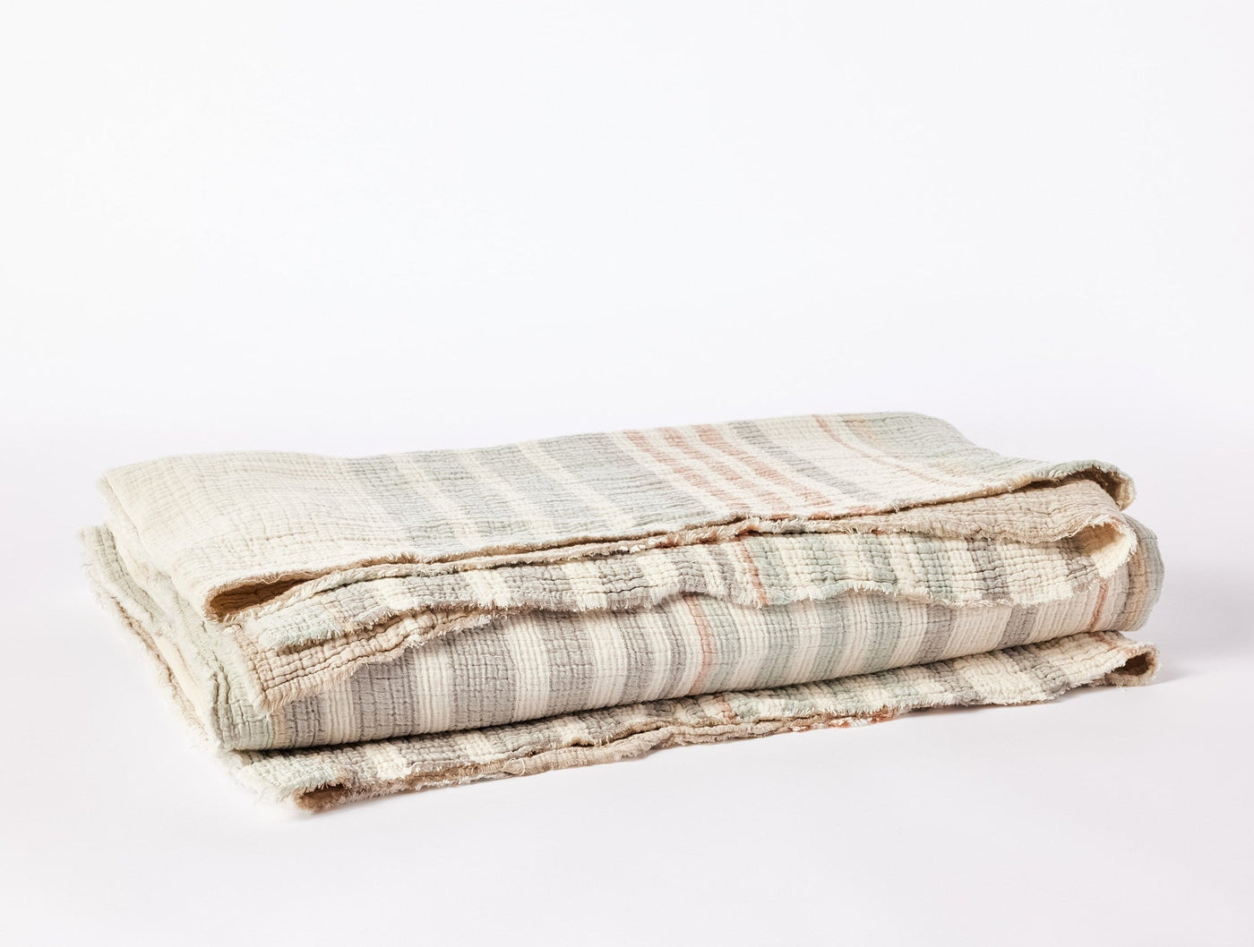 Close-up of folded Coyuchi Topanga Matelassé blanket showing striped weave texture in soft neutrals.