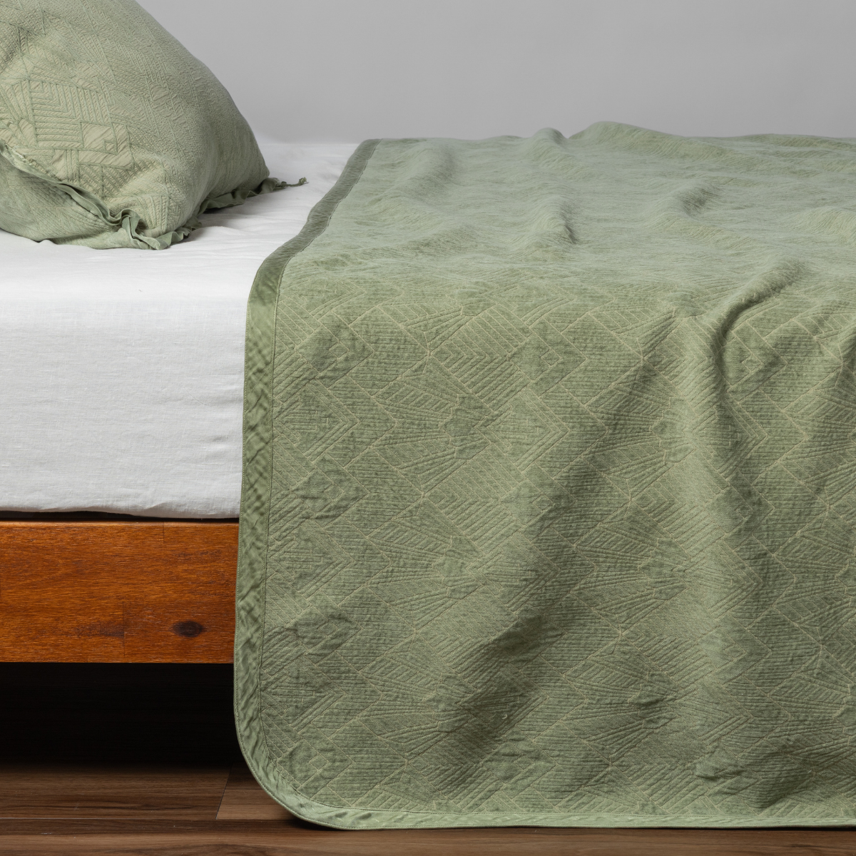 Bella Notte Trettino bedspread in Desert Sage draped over bed, showing geometric quilted pattern.