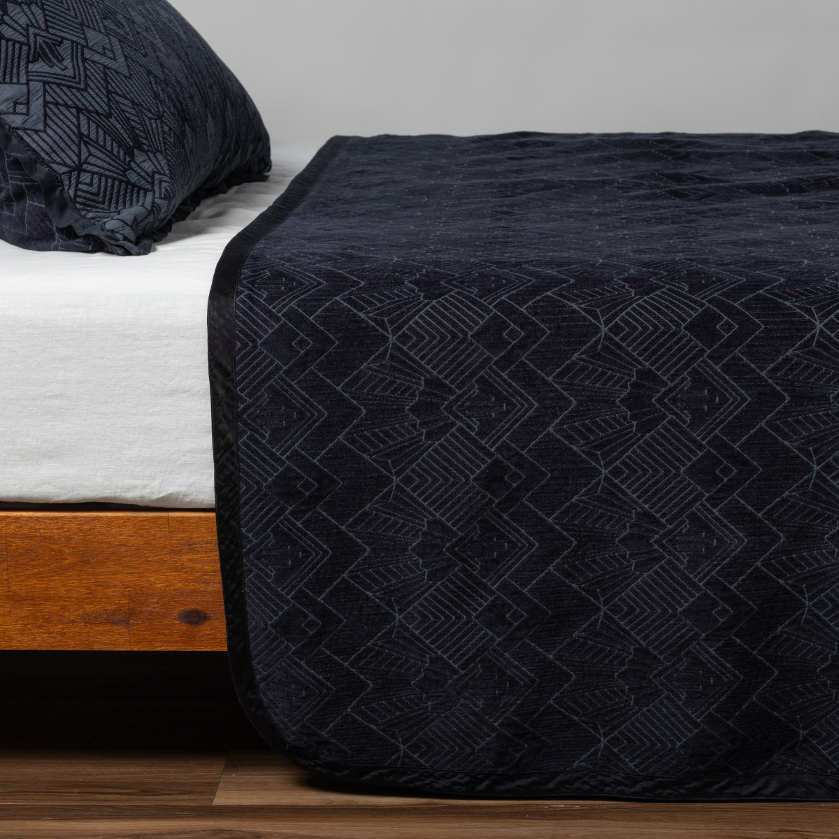 Slate Trettino bedspread draped over bed, showing geometric quilted pattern and matching sham.