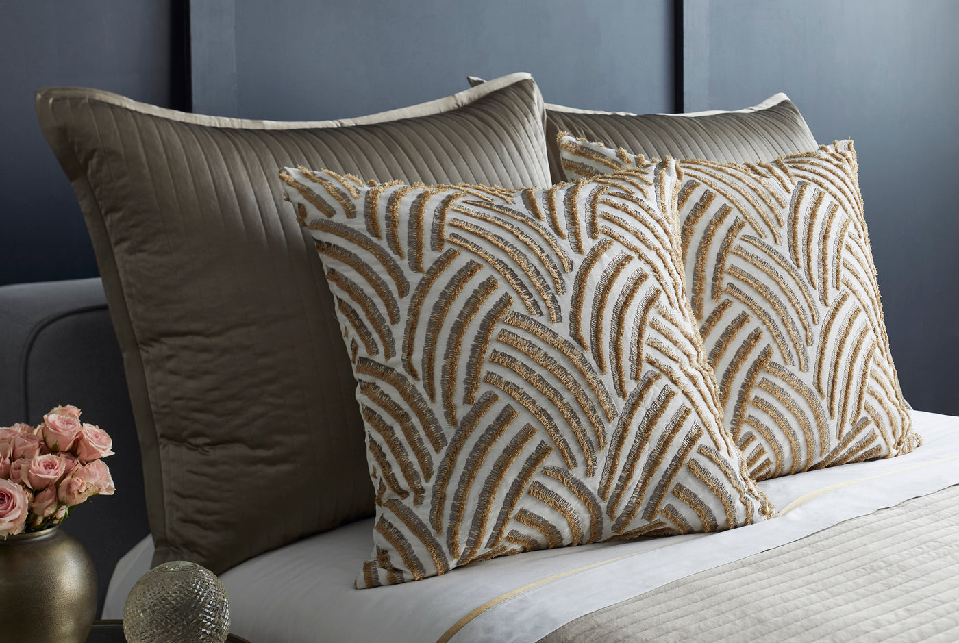 Ann Gish Trevi pillow in gold and ivory art deco fan pattern, styled on bed with taupe bedding.