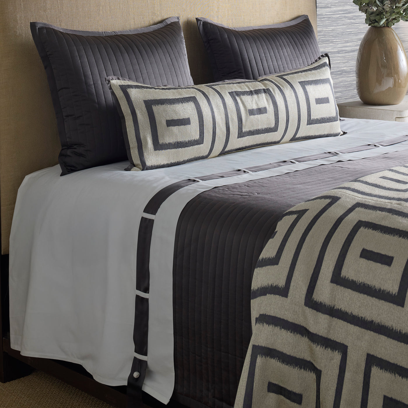 Long lumbar pillow with charcoal geometric maze pattern on ivory, styled on a layered gray bed.