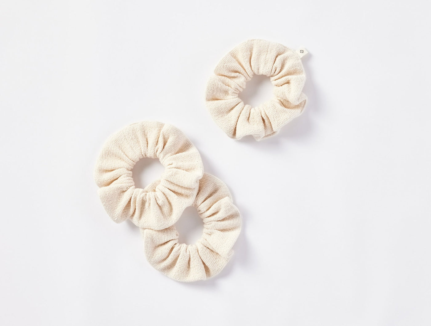 Coyuchi Bare scrunchie set of three, ivory textured linen fabric on white background.
