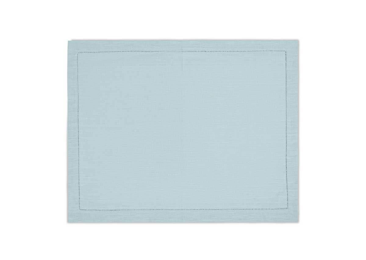 The Valentina Hemstitch Placemat Set by Matouk, shown in light blue with a subtle hemstitch border, is displayed flat against a white background.