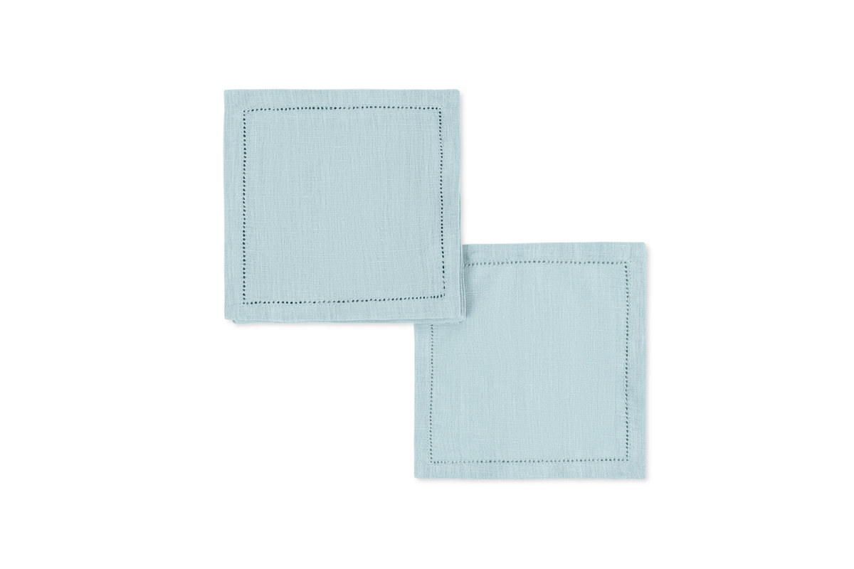 The Valentina Hemstitch Cocktail Napkin Set by Matouk features two light blue linen napkins with hemstitch borders—an elegant touch for any luxurious tabletop.