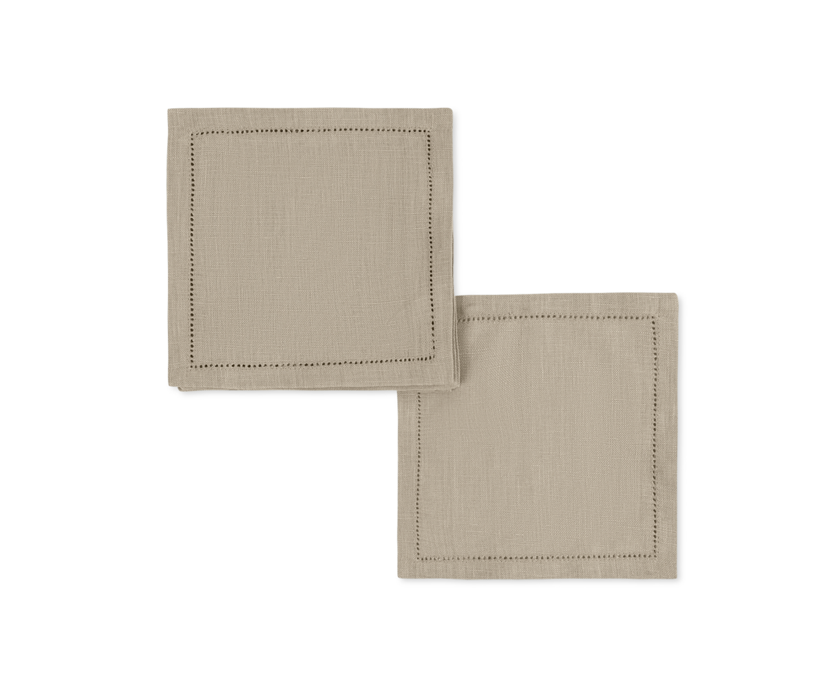 The Valentina Hemstitch Cocktail Napkin Set by Matouk features two beige linen napkins with a refined hemstitch border, arranged on a white background—an elegant choice for any luxurious tabletop.