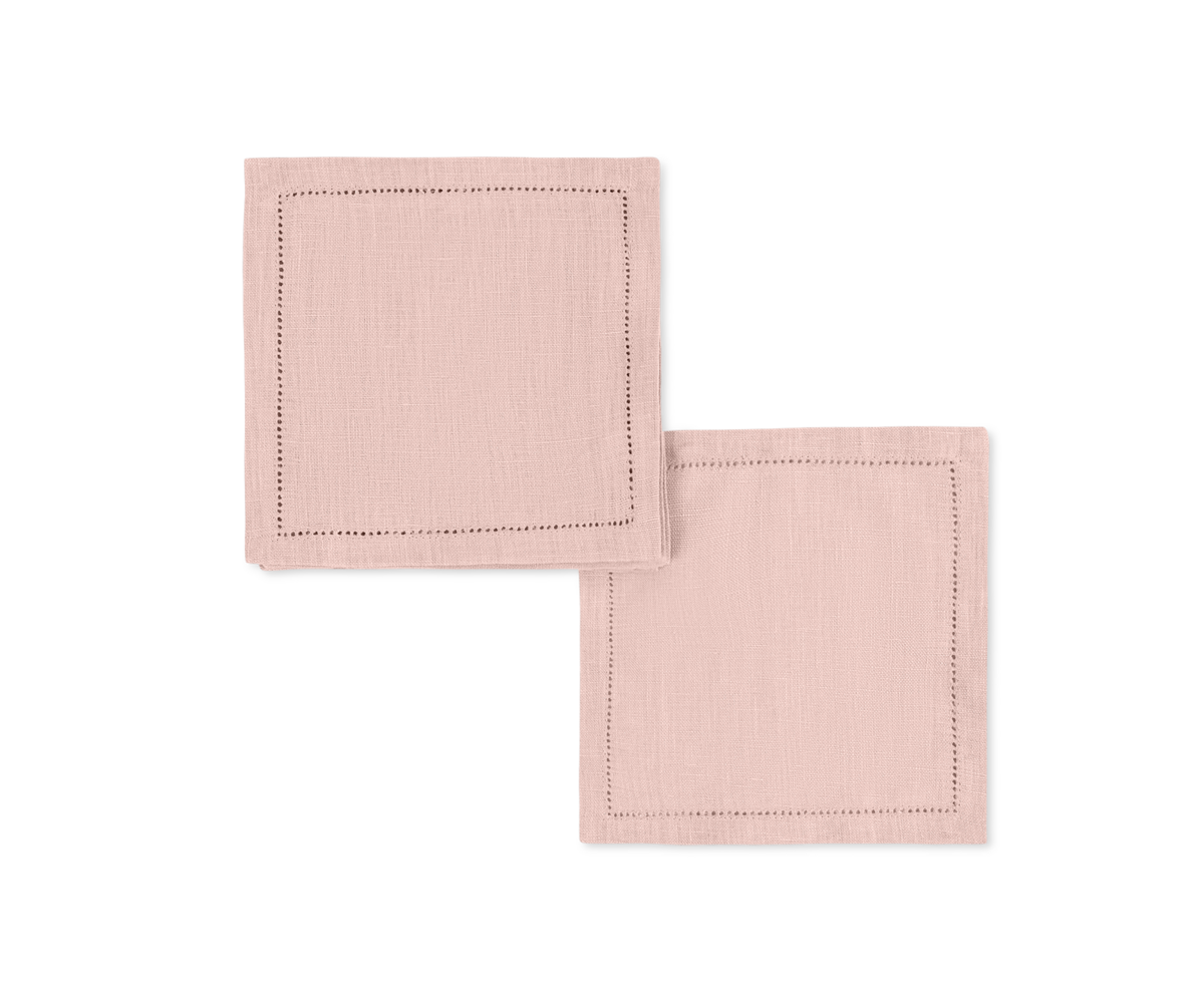 The Valentina Hemstitch Cocktail Napkin Set by Matouk, featuring two light pink linen napkins with delicate hemstitch borders, adds refined elegance to any luxurious tabletop.