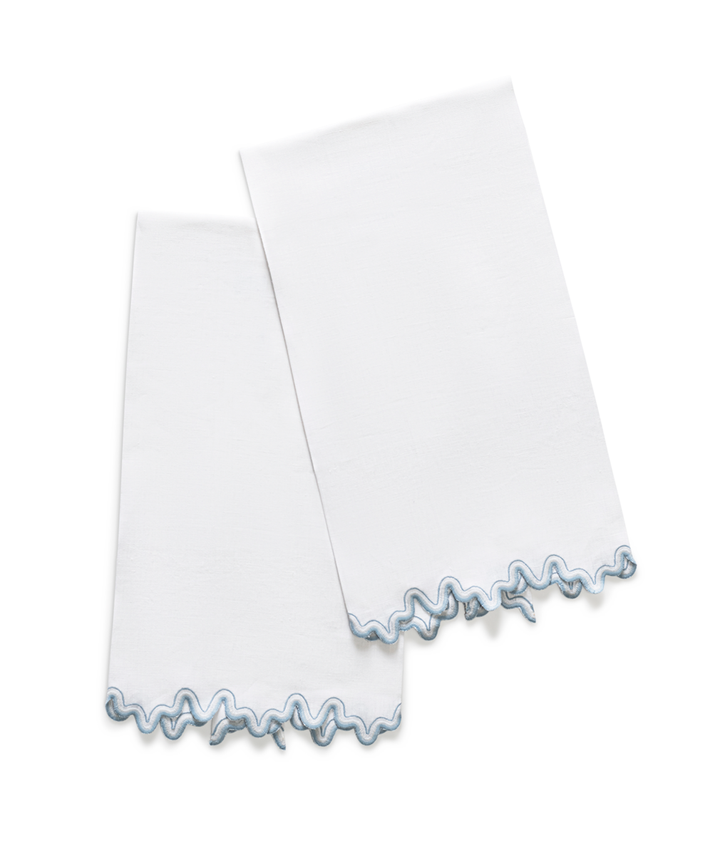 The Wave | Linen Guest Towel Set by Matouk features two white linen guest towels, each with a light blue wavy embroidered border—elegant accents for any table, displayed overlapping on a plain white background.