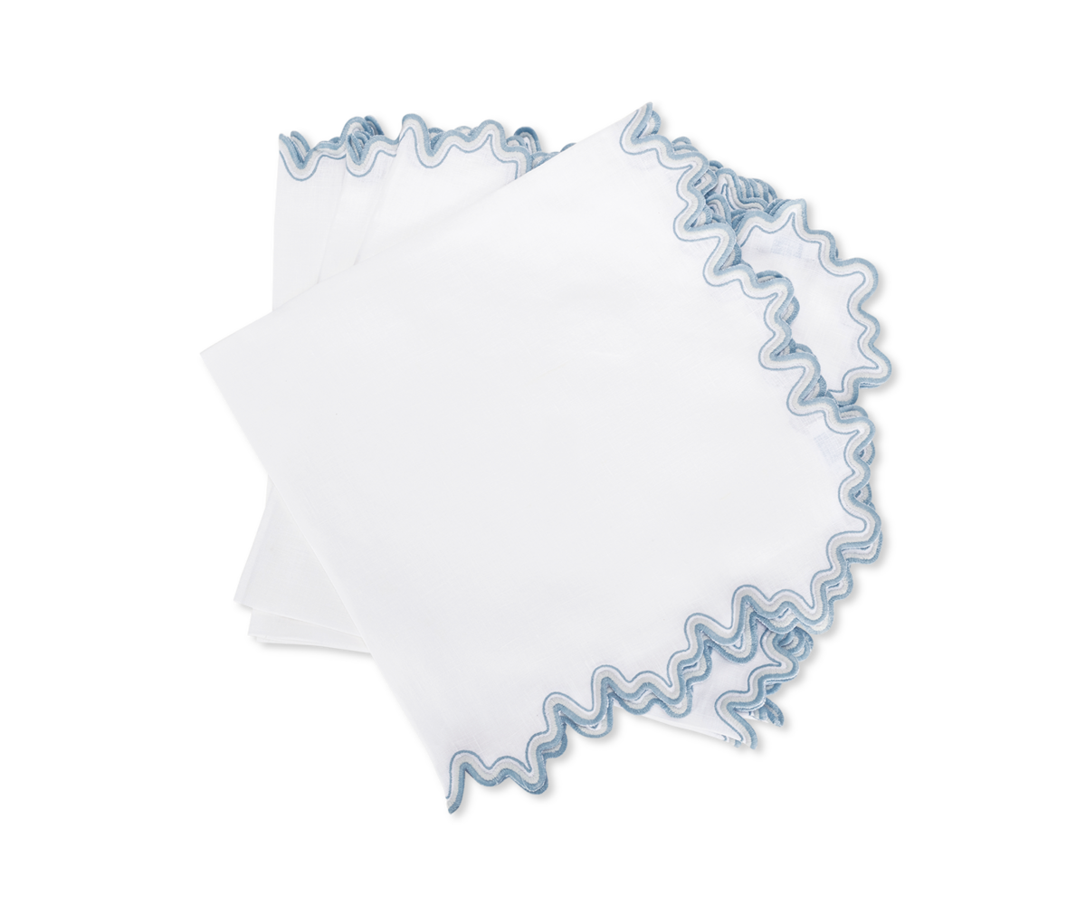 The Wave | Napkin by Matouk features white linen with wavy blue embroidered edges, adding elegance to your table setting. Perfect for any occasion, these stylish napkins bring sophistication to every meal.