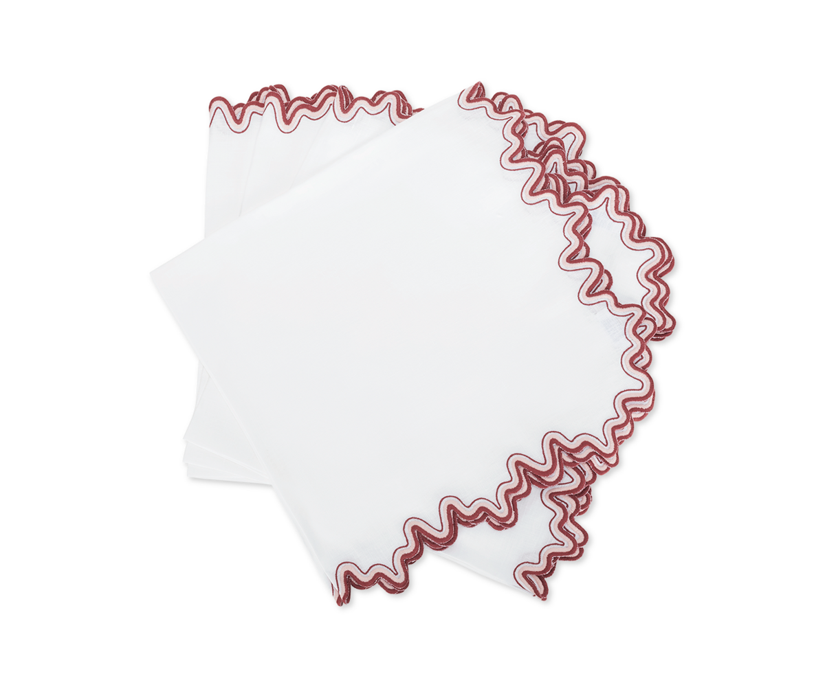 The Wave napkin by Matouk features folded white linen with wavy red embroidered edges, adding a touch of luxury to your dining space and displayed elegantly on a white background.