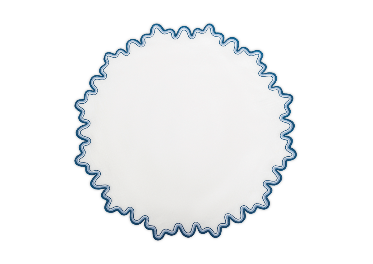 The Matouk Wave Placemat is a round white linen design with a blue wavy scalloped two-tone border, shown on a plain white background.