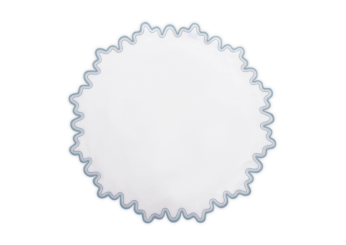 The Wave Placemat by Matouk is a round, white linen placemat featuring a wavy blue two-tone embroidered border, shown from above on a plain background.