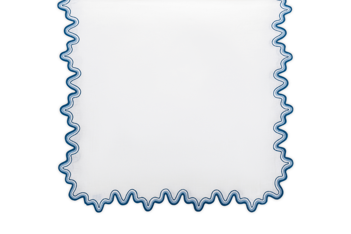 The Matouk Wave Tablecloth Runner is a white rectangular linen with a wavy two-tone embroidered border, shown on a plain background.