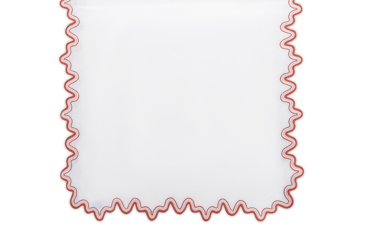 The Matouk Wave Tablecloth Runner is a white rectangular piece with a luxurious linen feel, featuring a wavy, two-tone red border along the edges.
