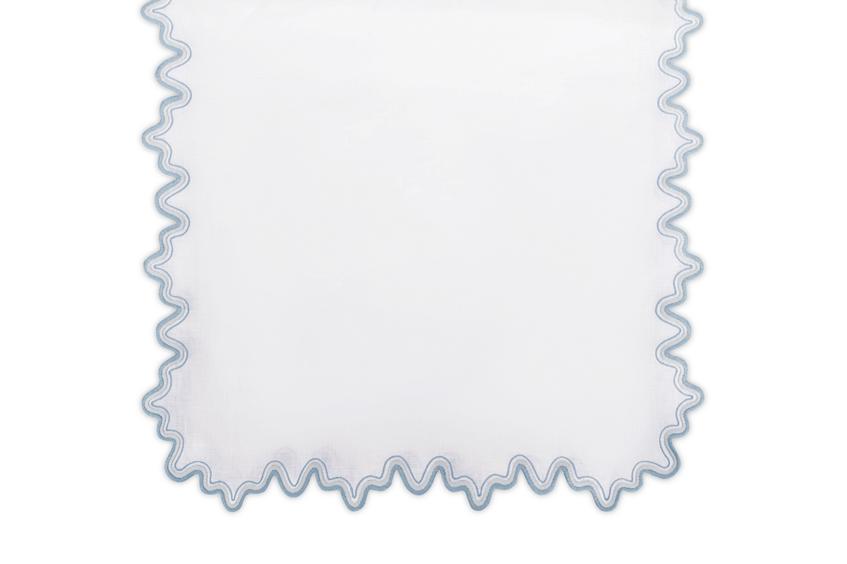 The Matouk Wave Tablecloth Runner features white luxurious linen with a wavy blue two-tone embroidered border, elegantly displayed against a plain background.