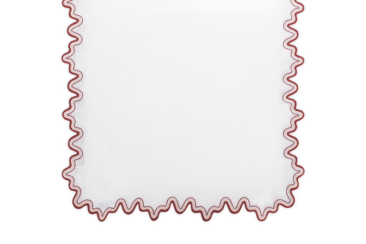 The Matouk Wave Tablecloth Runner features a luxurious linen design with a wavy red scalloped two-tone border, perfect for an elegant embroidered tabletop setting.