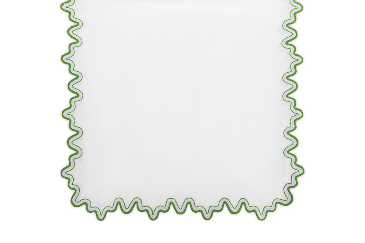The Matouk Wave Tablecloth Runner features a luxurious white linen texture and a green wavy two-tone border around the edges.