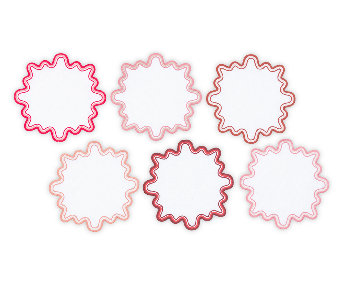 The Matouk Wave Cocktail Napkin Set features six round, white napkins with wavy edges, a pink and red two-tone border, and a luxurious linen look, arranged in two rows on a light background.