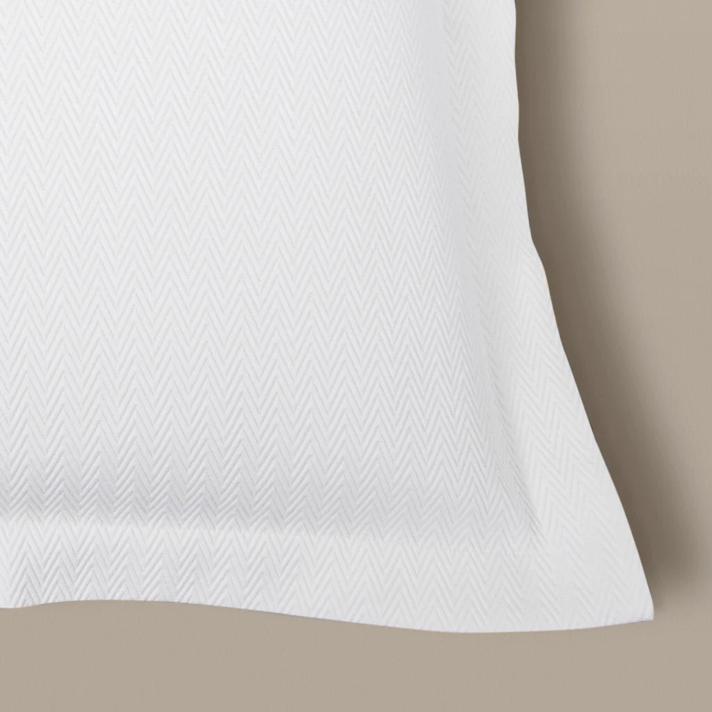 Close-up of the Waves | Pique Euro Sham Set by Frette, featuring a subtle chevron pattern in white cotton, displayed on a beige surface—ideal for hotel hospitality.