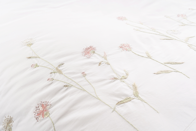 Close-up of ivory cotton bedding with delicate pink and sage embroidered wildflowers.