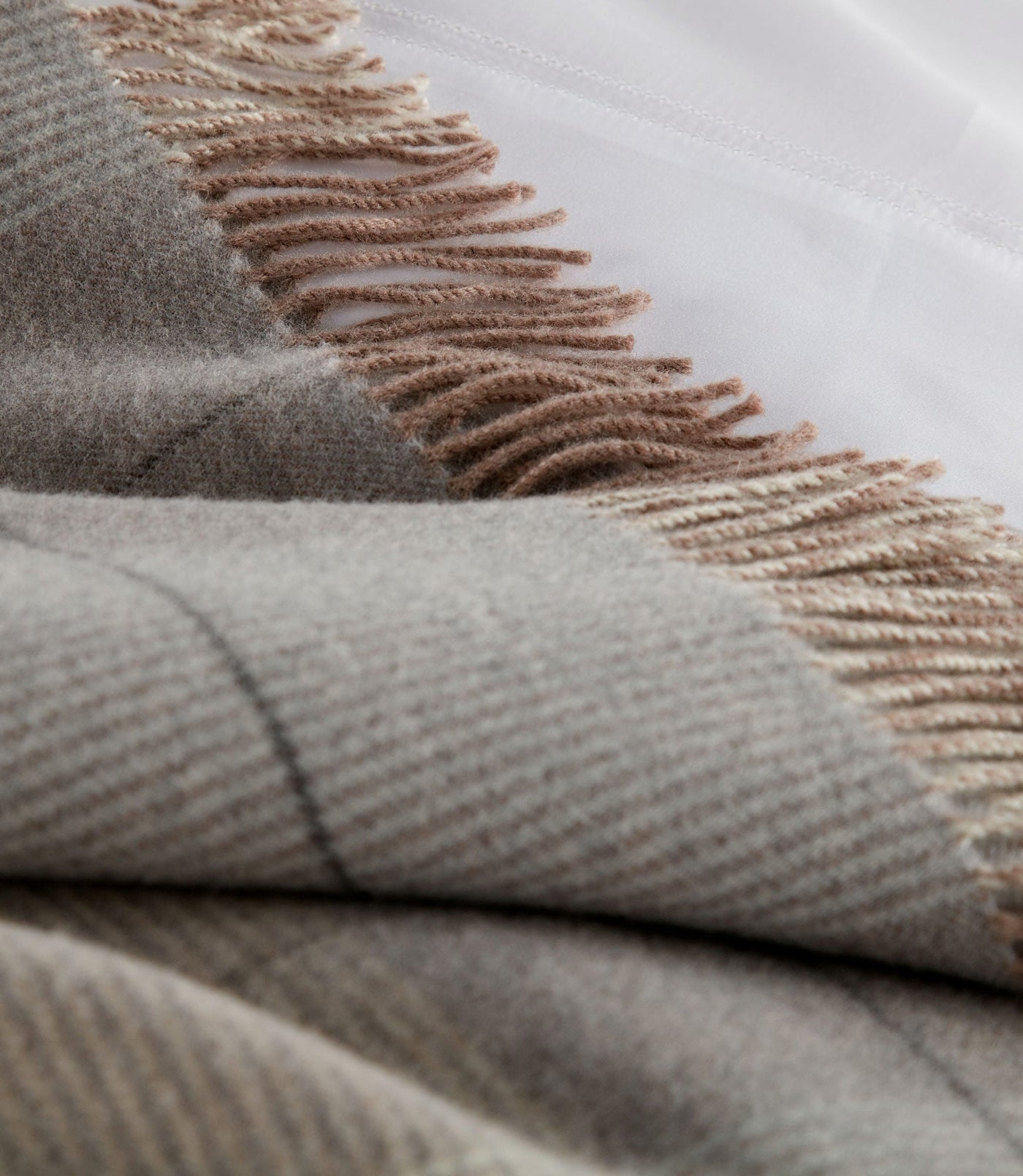 Close-up of York throw fringe detail in taupe and blush against folded grey wool.